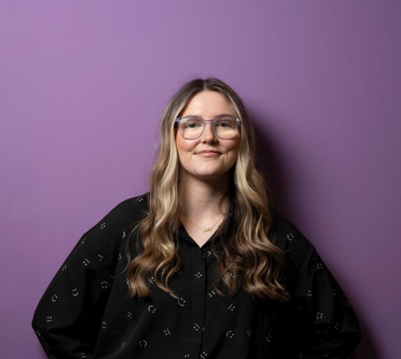 Beth Smiling whilst leaning against a purple wall